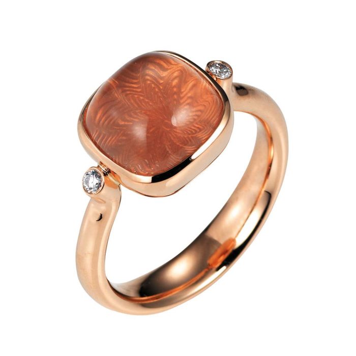 Gold ring with peach coloured gemstone on guilloched surface with diamonds