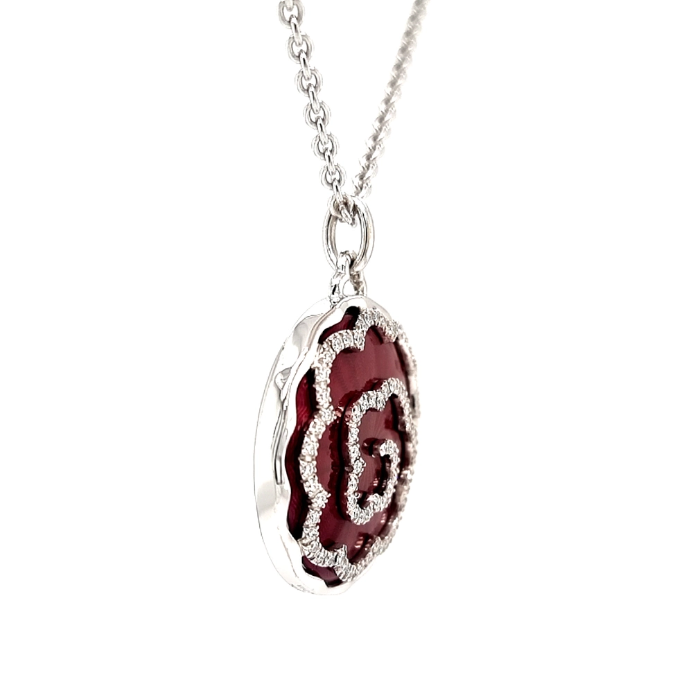 A round pendant on a chain. It is made of white gold and about the size of a large coin. The surface shines in a rich ruby-red colour with a wavy pattern. Across it runs a large flower shape made of many small diamonds. The pendant hangs from a fine chain.