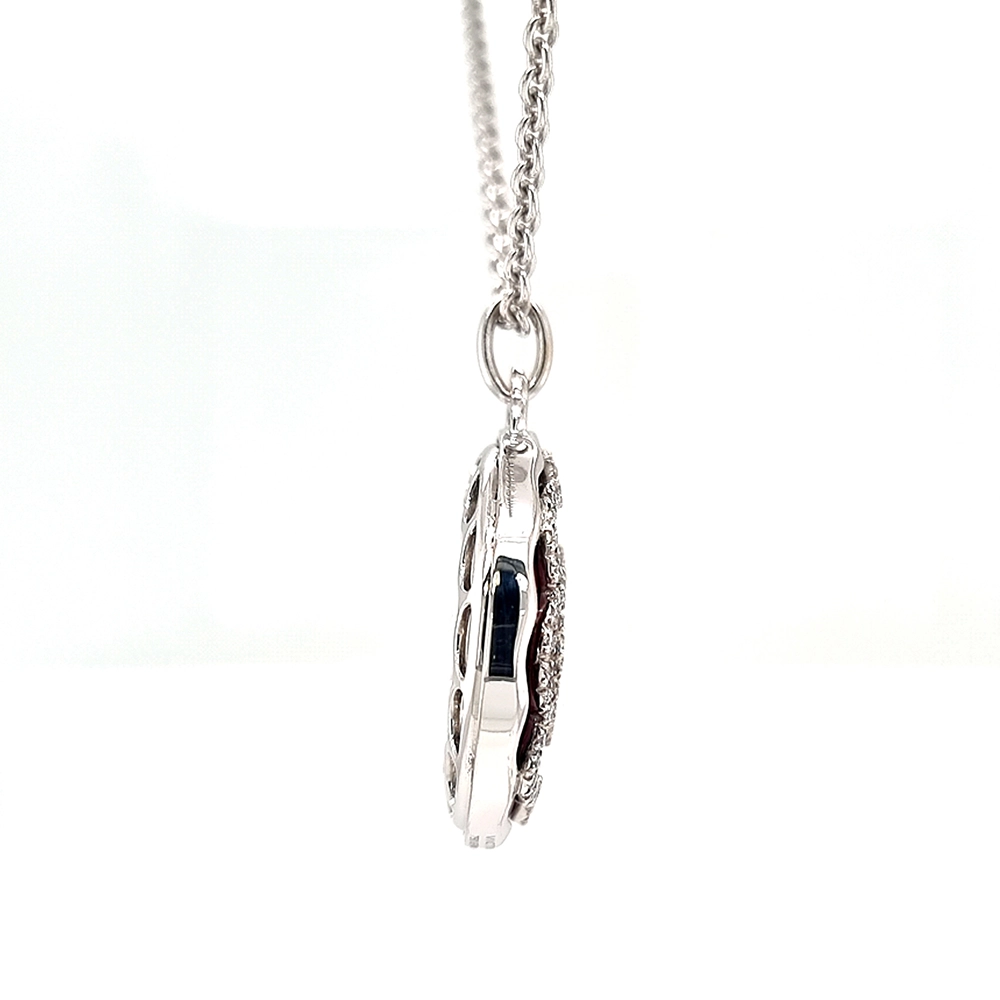 A round pendant on a chain. It is made of white gold and about the size of a large coin. The surface shines in a rich ruby-red colour with a wavy pattern. Across it runs a large flower shape made of many small diamonds. The pendant hangs from a fine chain.