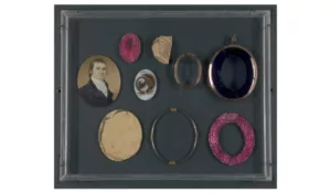 A rectangular frame features 8 components of a disassembled locket penant including a miniature portrait and hair.