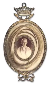 Oval locket pendant containing a man's portrait and lock of hair. Top decorated with a crown and the bottom features a bow.