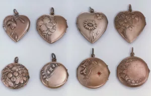4 heart and four round locket pendants arranged in two rows all of them featuring floral motives and one with a round red gemstone.