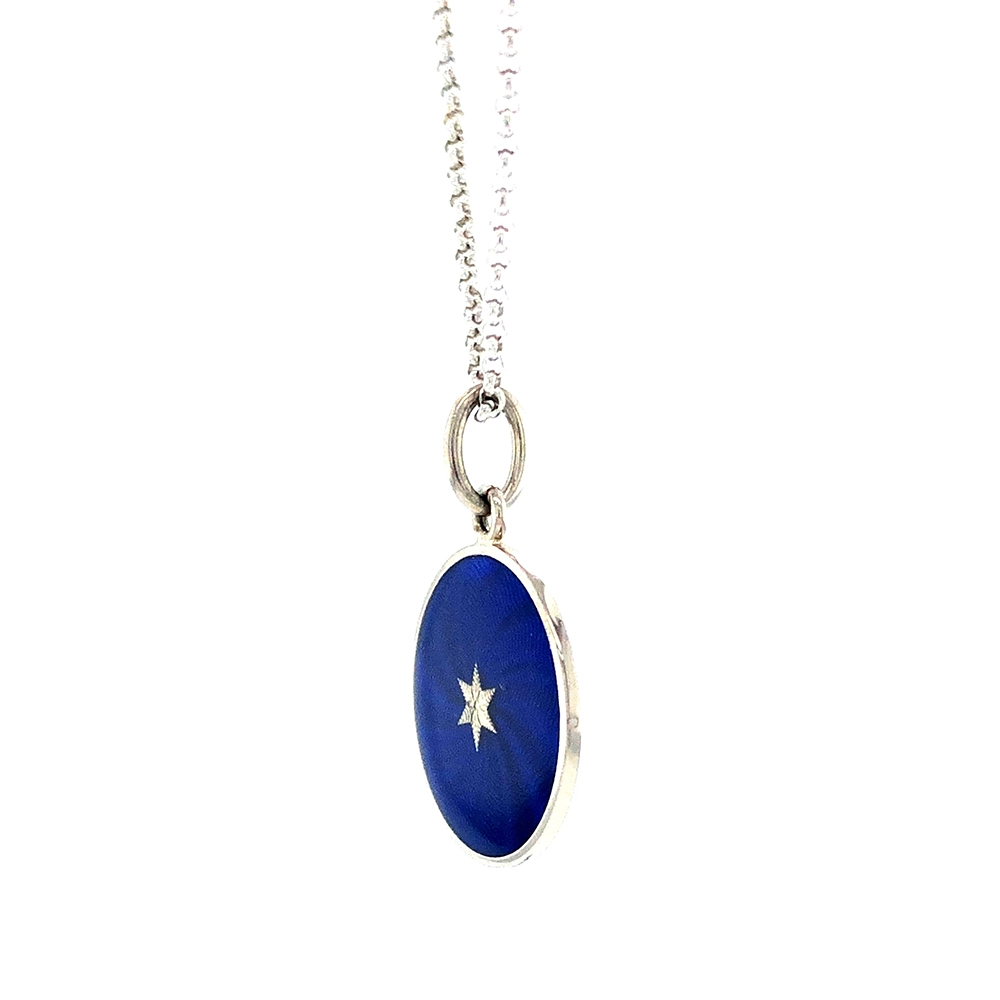 Small round pendant made of white gold, about the size of a small coin. The front shimmers in electric blue translucent enamel with a fine wave pattern. At the center lies a tiny hexagonal gold insert shaped as a star with microscopic relief details.
