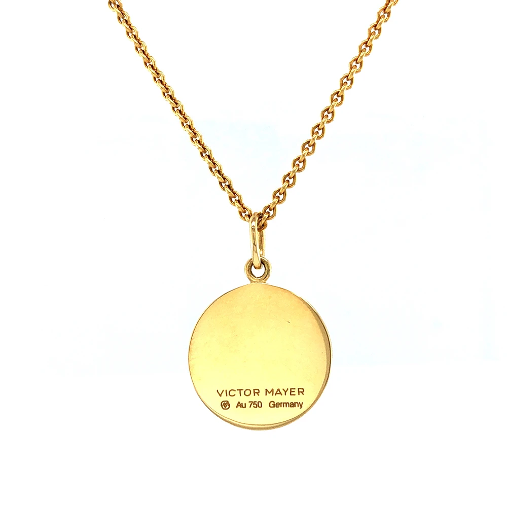 Small round pendant made of yellow gold, about the size of a small coin. The front shimmers in opalescent white, shifting colours like an opal when catching the light. A fine wave pattern appears beneath the enamel.