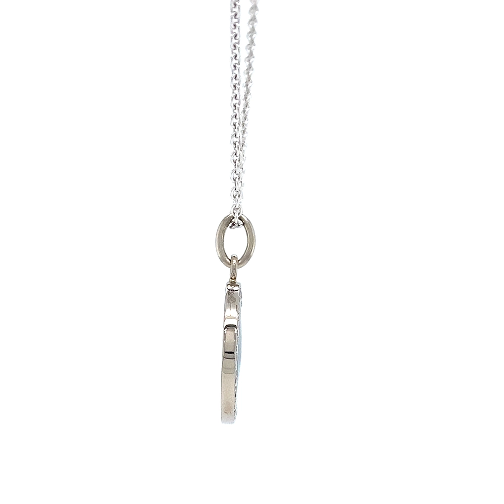 Small round pendant made of white gold, about the size of a small coin. The front shimmers turquoise in translucent enamel with a fine wave pattern. At the center lies a tiny hexagonal star-shaped gold insert, surrounded by 24 sparkling diamonds.