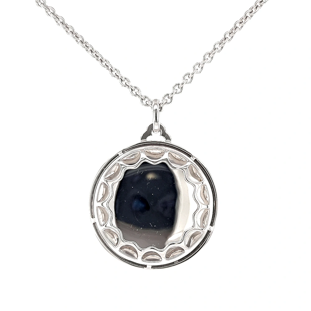 A round pendant on a chain. It is made of white gold and about the size of a large coin. The surface shines in a rich golden-amber colour with a wavy pattern. Across it runs a large flower shape made of many small diamonds. The pendant hangs from a fine chain.