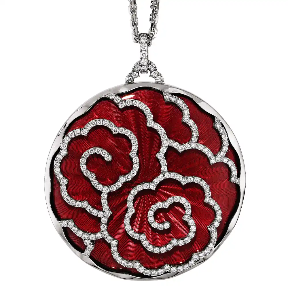 A round pendant on a chain. It is made of white gold and about the size of a large coin. The surface shines in a rich ruby-red colour with a wavy pattern. Across it runs a large flower shape made of many small diamonds. The pendant hangs from a fine double chain.