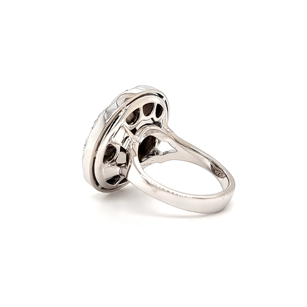 Ein Ring aus Weißgold mit einem runden Ringkopf. Dieser hat die Größe einer großen Münze. Die Oberfläche des Ringkopfes schimmert in einem kräftigen Rubinrot-Ton mit einem wellenartigen Muster. Darüber liegt die Form einer großen Blüte, besetzt mit vielen kleinen Diamanten.