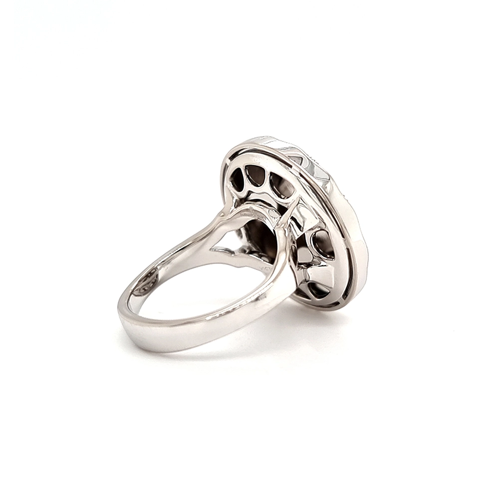 Ein Ring aus Weißgold mit einem runden Ringkopf. Dieser hat die Größe einer großen Münze. Die Oberfläche des Ringkopfes schimmert in einem kräftigen Rubinrot-Ton mit einem wellenartigen Muster. Darüber liegt die Form einer großen Blüte, besetzt mit vielen kleinen Diamanten.