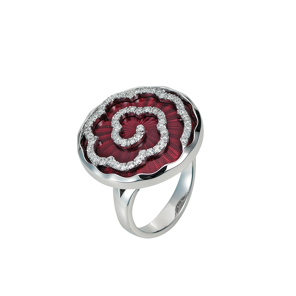 Ein Ring aus Weißgold mit einem runden Ringkopf. Dieser hat die Größe einer großen Münze. Die Oberfläche des Ringkopfes schimmert in einem kräftigen Rubinrot-Ton mit einem wellenartigen Muster. Darüber liegt die Form einer großen Blüte, besetzt mit vielen kleinen Diamanten.