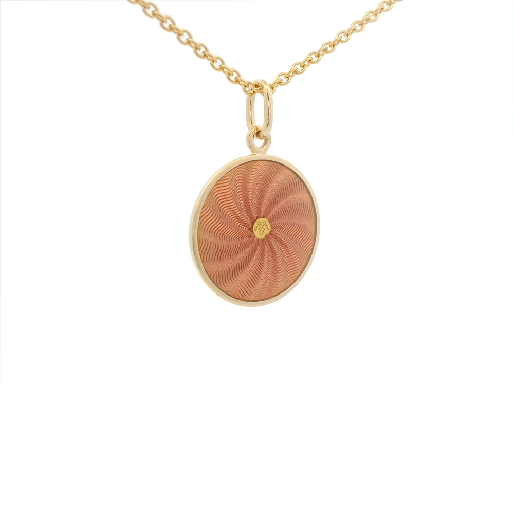 Kleiner runder Anhänger aus Gelbgold, etwa so groß wie eine kleine Münze. Die Vorderseite schimmert rosa in durchscheinender Emaille mit feinem Wellenmuster. In der Mitte ist ein winziges sechseckiges Goldplättchen eingelassen, das die Buchstaben V und M als Relief zeigt.