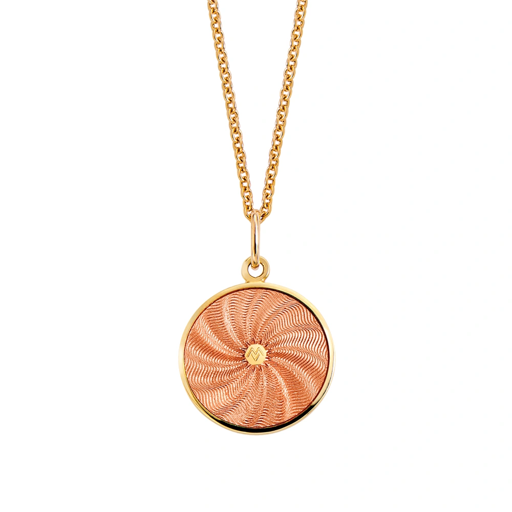 Kleiner runder Anhänger aus Gelbgold, etwa so groß wie eine kleine Münze. Die Vorderseite schimmert rosa in durchscheinender Emaille mit feinem Wellenmuster. In der Mitte ist ein winziges sechseckiges Goldplättchen eingelassen, das die Buchstaben V und M als Relief zeigt.