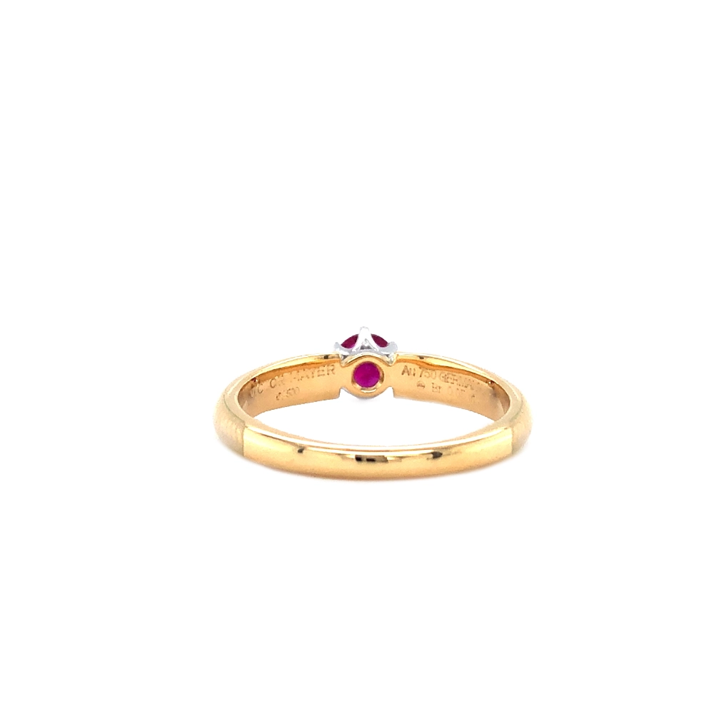 Goldener Ring mit einem roten Mittelstein und zwei Reihen kleiner Diamanten daneben. Die Ringschultern sind weiß gefärbt.