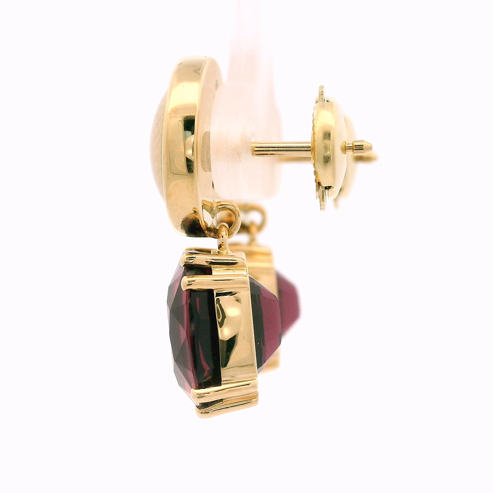 Pair of yellow-gold earrings with red cushion-cut rhodolites in four-claw settings and round white enamel boutons with gold rims.