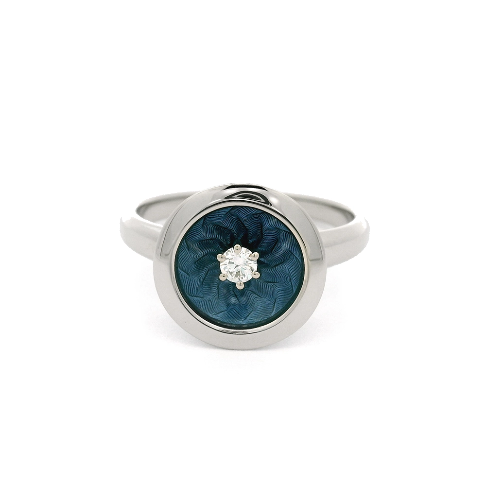 Ring aus Weißgold mit rundem Ringkopf. Der Ringkopf ist konkav gewölbt und mit mediumblauer transluzider Feueremaille versehen, unter der ein feines Windmühlen-Guilloché sichtbar ist. Im Zentrum der Emaillefläche sitzt ein einzelner kleiner Brillant als klarer Lichtpunkt. Die Gestaltung wirkt ruhig, geometrisch und ausgewogen.